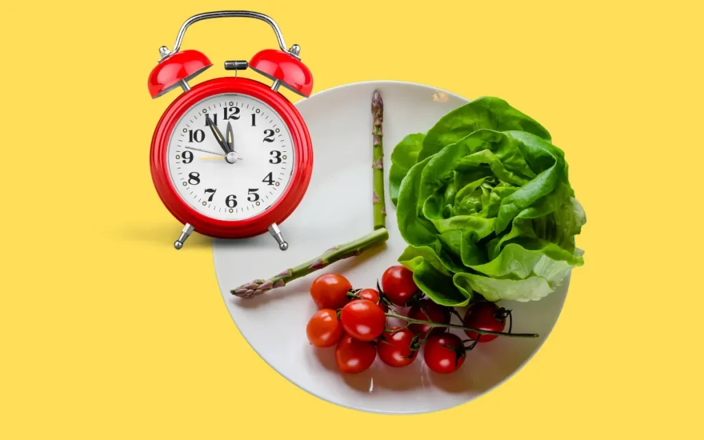 Jejum Intermitente: 5 Dicas Especiais Para Iniciar -Verduras e legumes, em uma parte do prato, com um relógio vermelho ao lado.