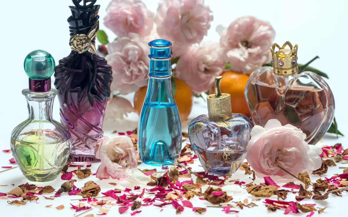 Perfume Importado Feminino: Glamour a seu Dispor - frascos de perfume coloridos em cima de uma mesa com pétalas de rosa.