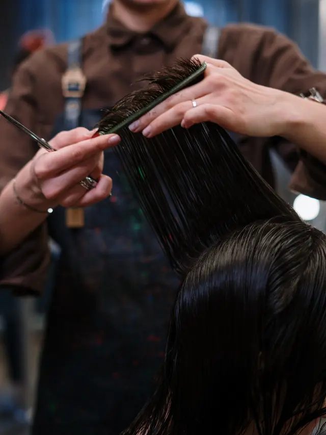 Cabeleireira cortando o cabelo de uma mulher, segurando a tesoura e o pente.