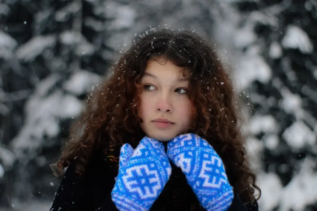 Mulher com roupa de frio, usando luvas, com um pouco de neve nos cabelos