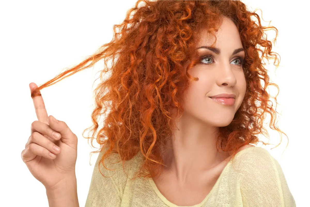 Nutrição Capilar Cabelos Mais Bonitos e Saudáveis - Mulher ruiva cacheada segurando um cacho do seu cabelo