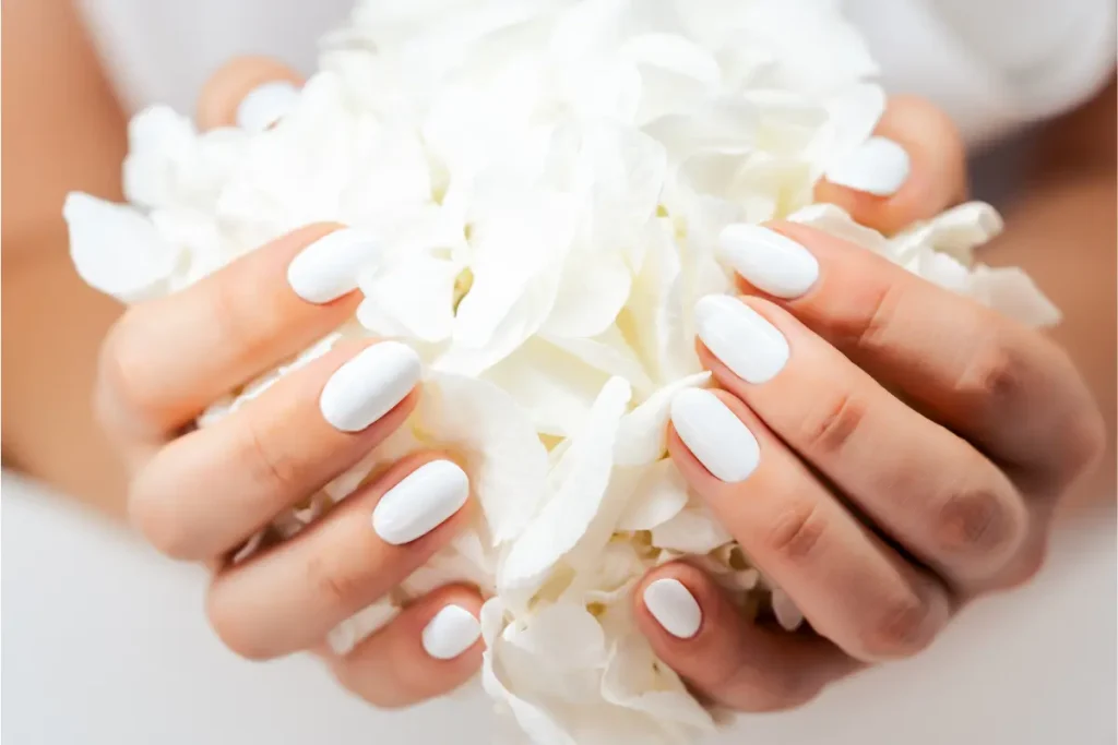 Mãos com unhas pintadas de branco segurando flores brancas