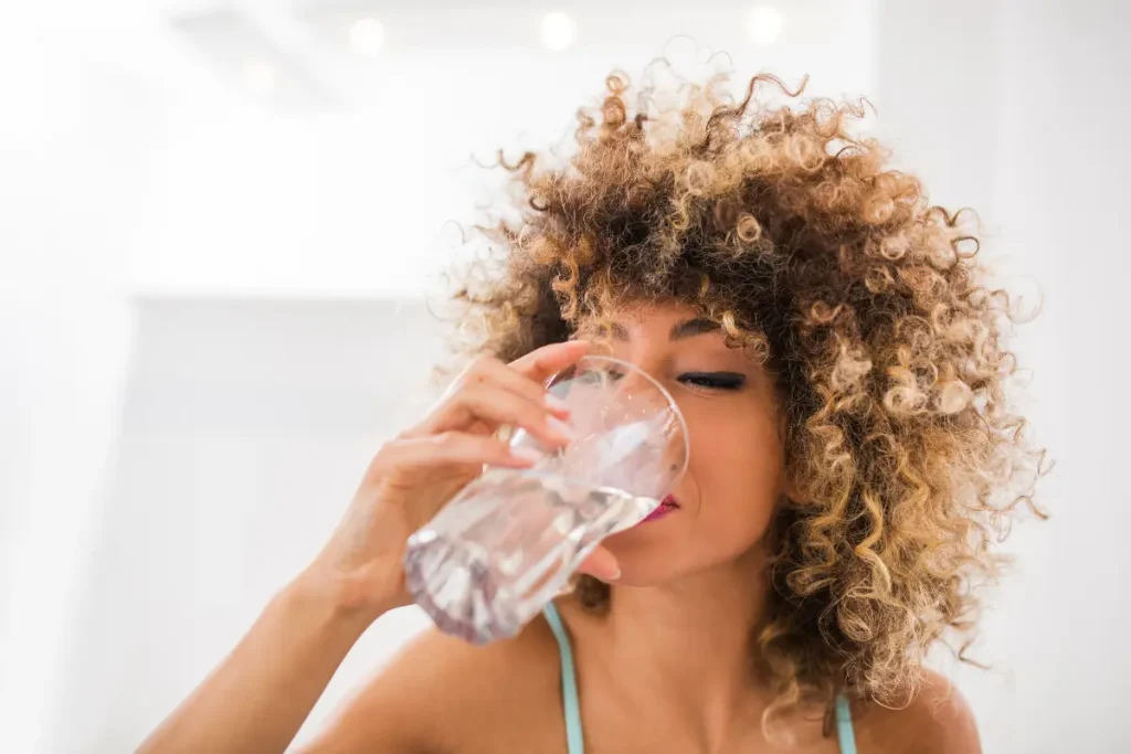 Mulher bebendo água com um copo de vidro transparente