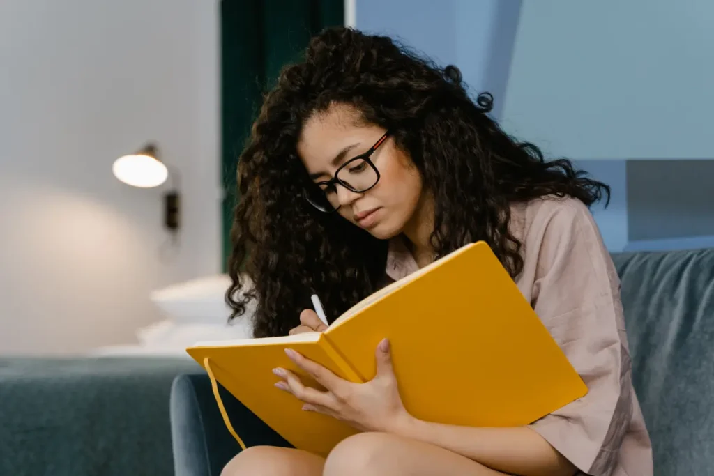 Mulher escrevendo num caderno amarelo