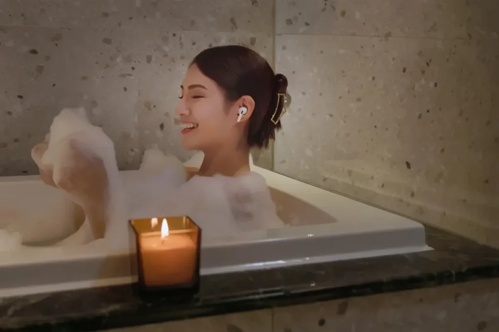 Mulher feliz tomando banho na banheira, escutando música com um fone de ouvido