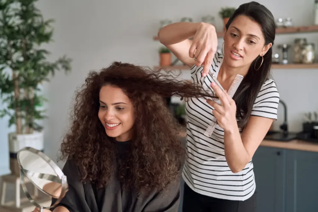 Cabeleireira cortando o cabelo cacheado de uma cliente