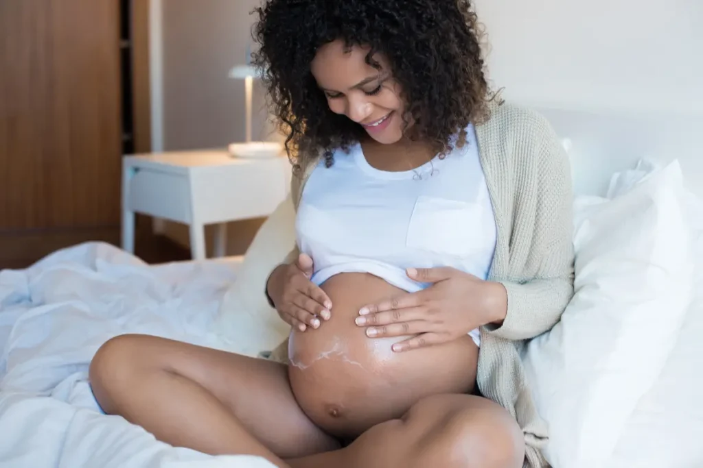 Mulher grávida passando creme hidratante na barriga