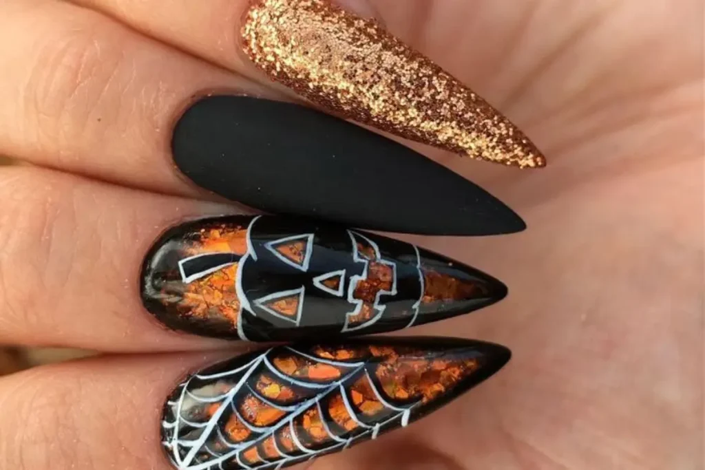 Unhas pintadas de preto e dourado decoradas com abóbora e teia de aranha