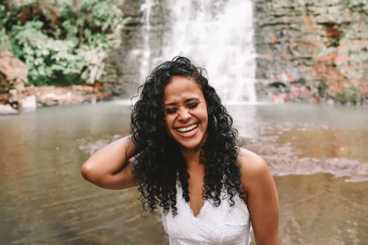 8 Hábitos Saudáveis Para Começar o Ano Com Mais Saúde - Mulher na beira de uma cachoeira sorrindo