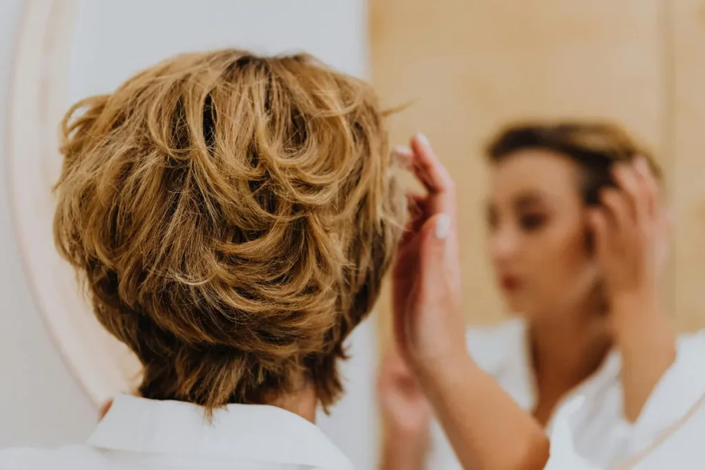 Mulher se olhando no espelho e arrumando o cabelo