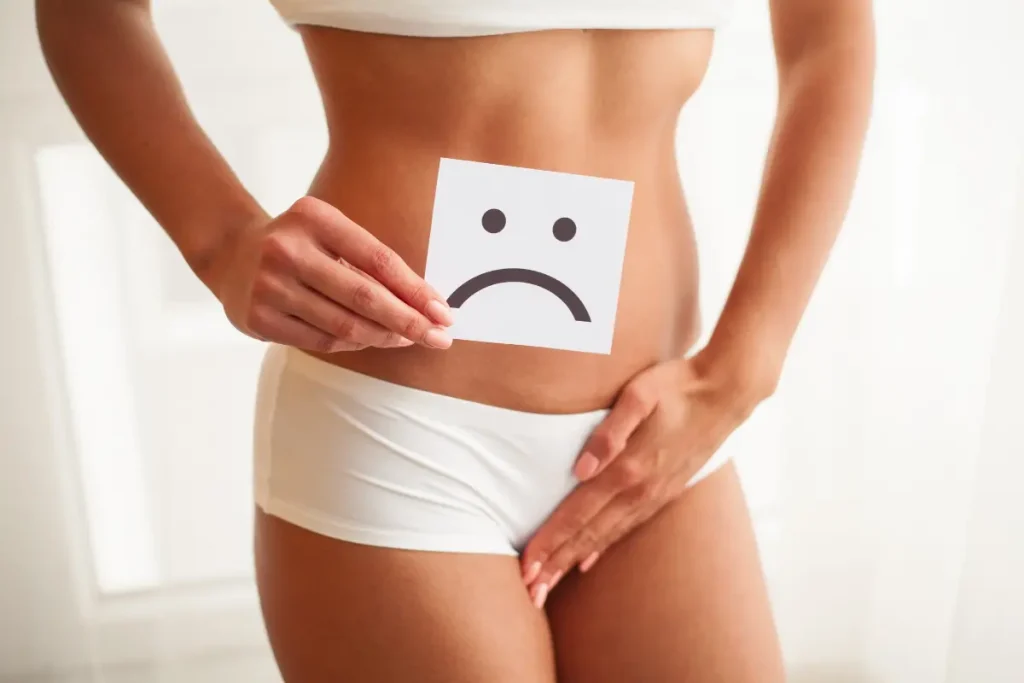 Mulher segurando uma plaquinha com expressão de triste e a outra mão está em frente as suas partes íntimas