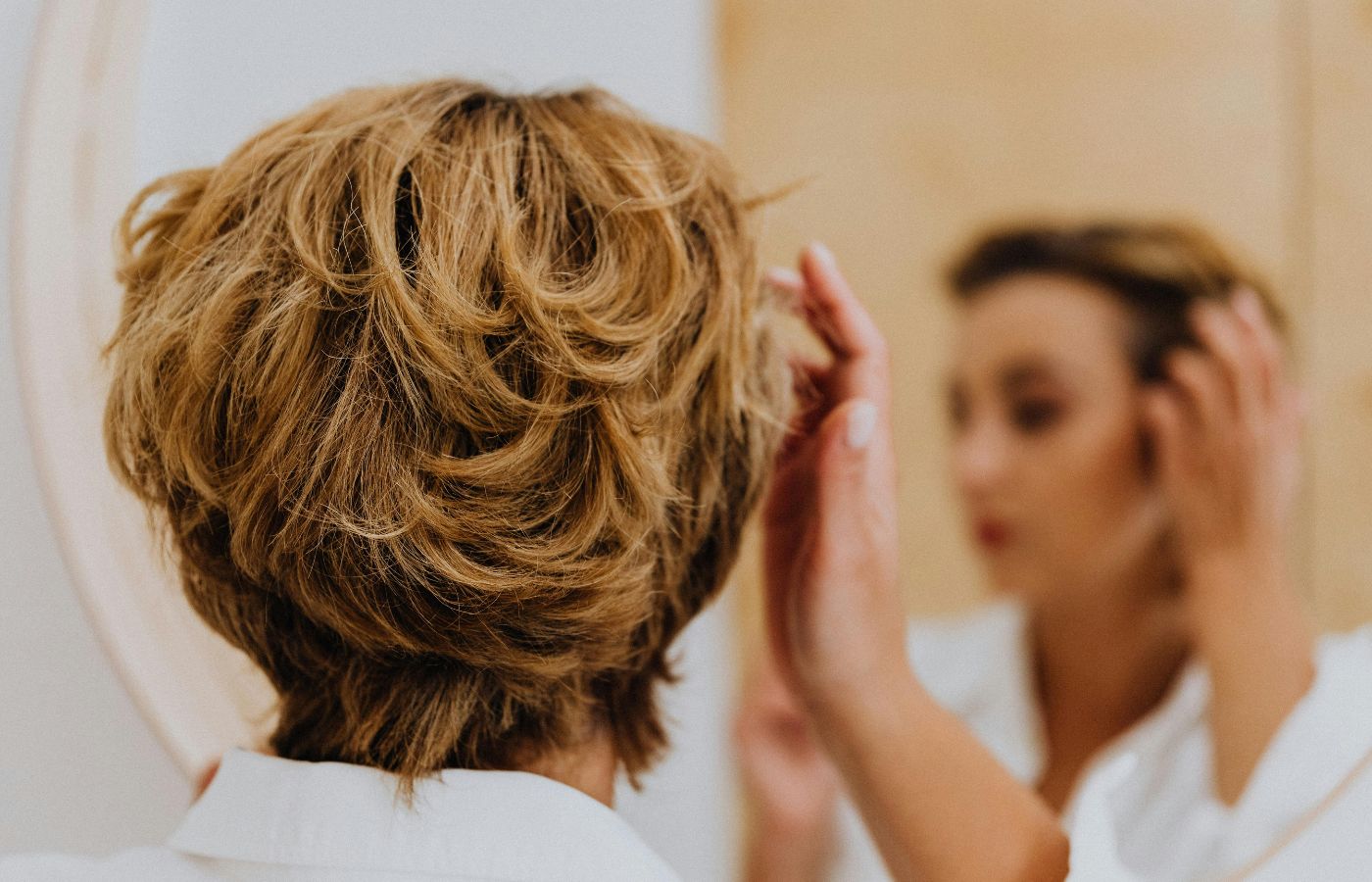Mulher com a mão no cabelo se olhando no espelho
