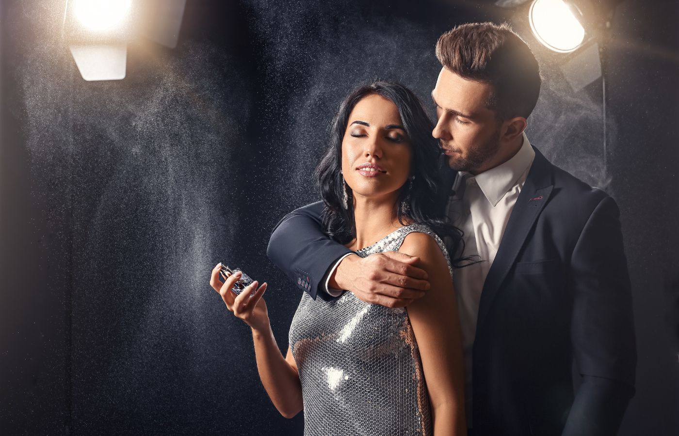 Homem abraçado numa mulher que está passando perfume